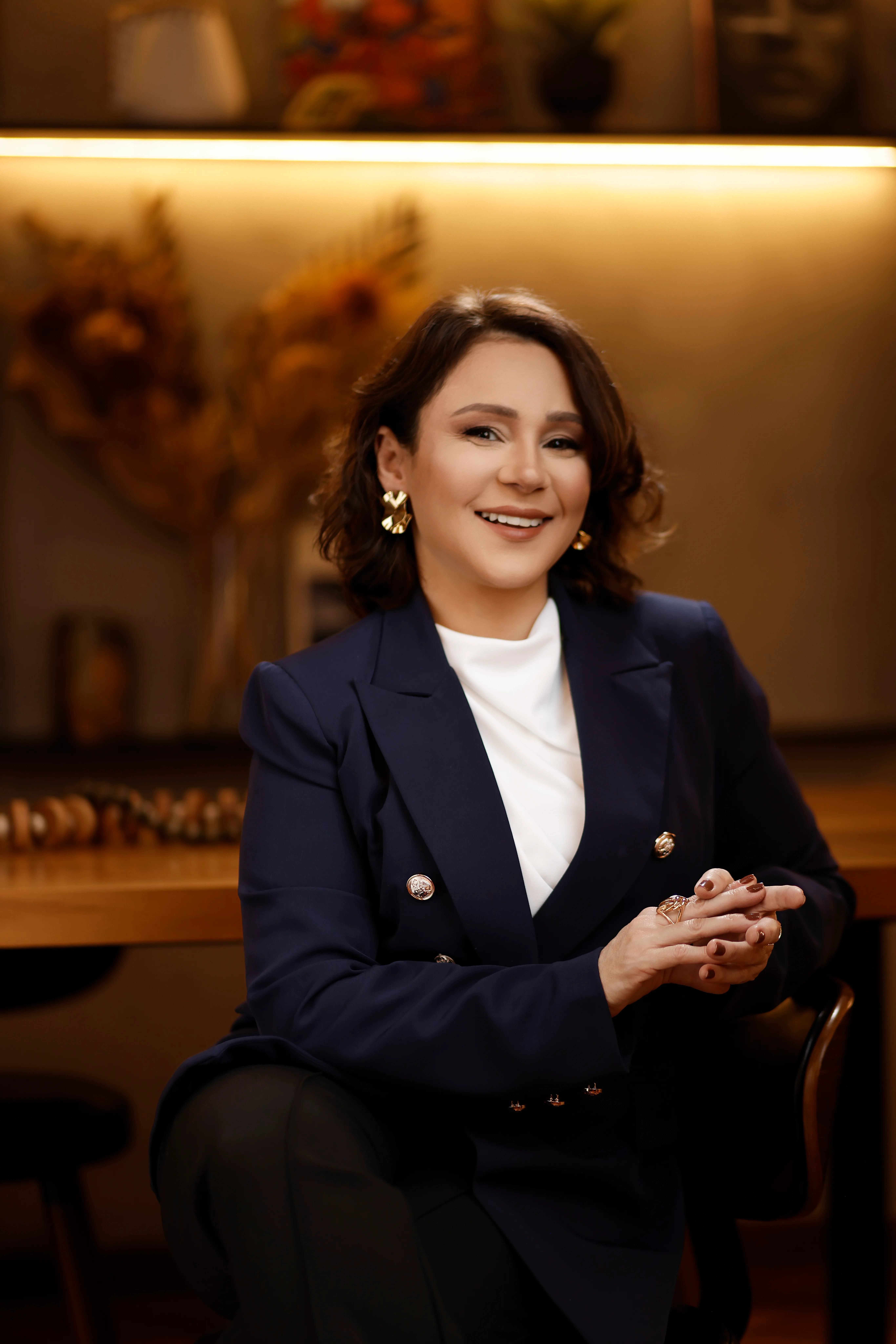 Katiuscia Silva, de blazer azul-marinho, sentada à mesa de reunião, sorrindo com expressão confiante e acessível.