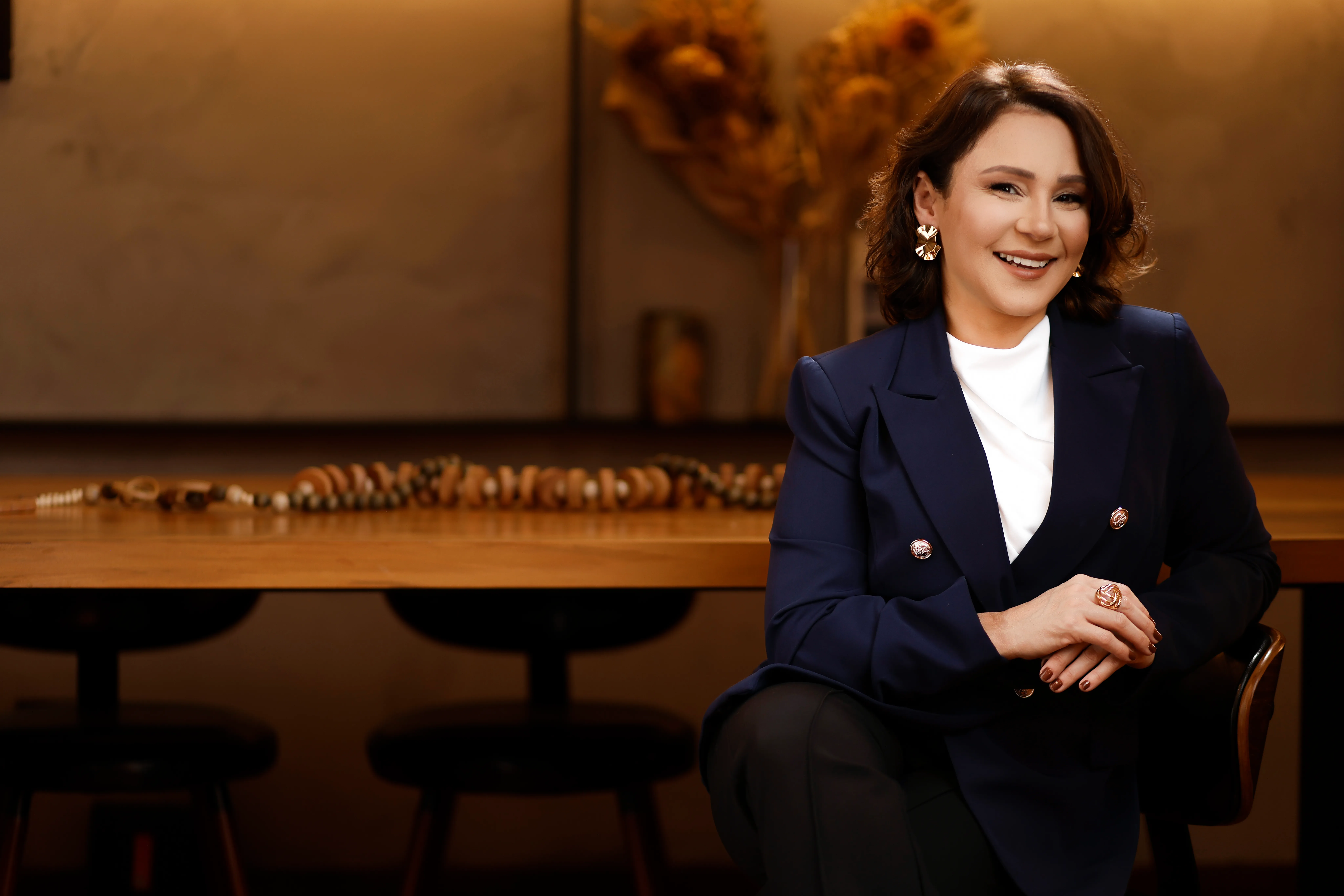 Katiuscia Silva sorrindo, sentada à mesa de reunião em plano aberto.