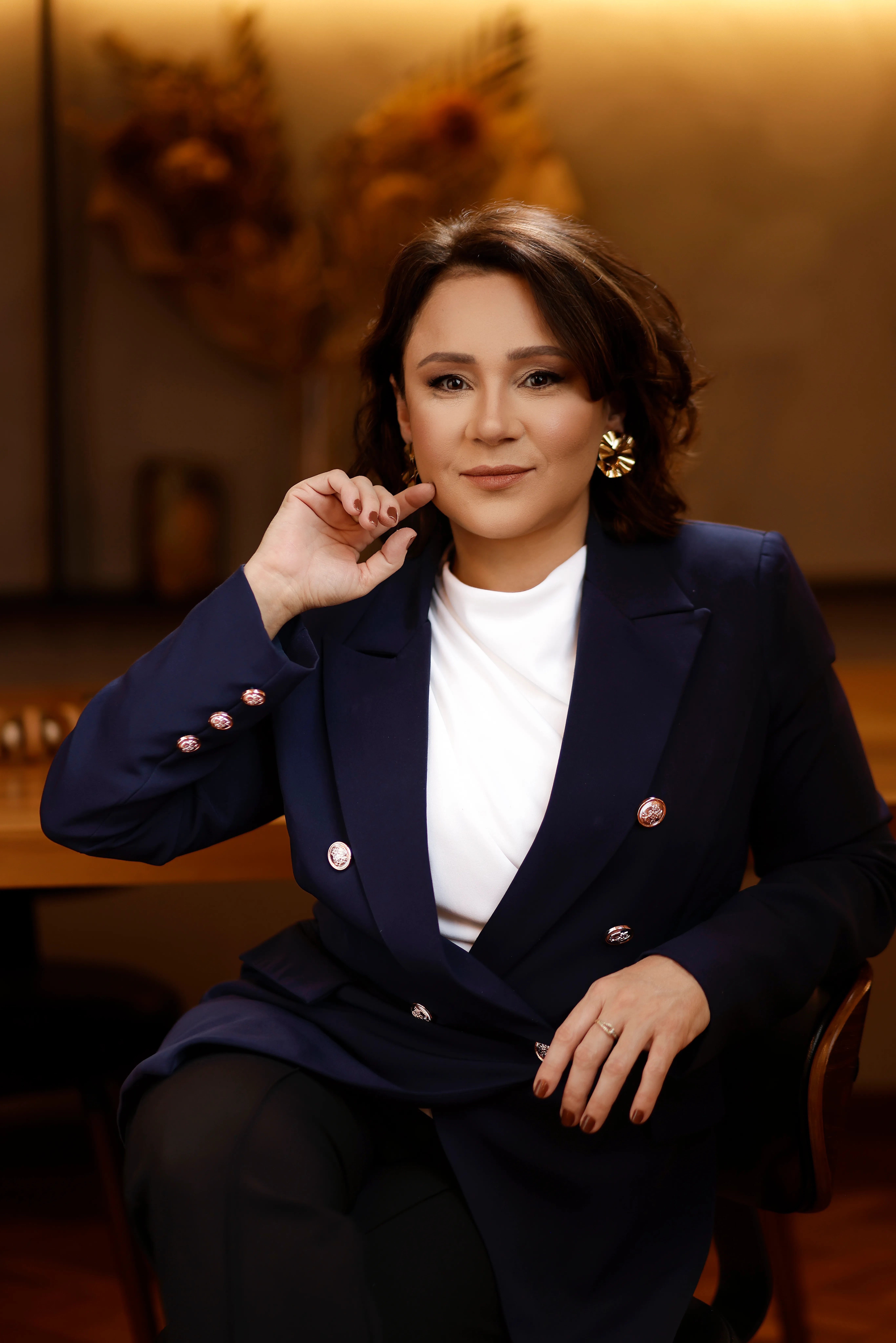 Katiuscia Silva, de blazer azul-marinho, com a mão próxima ao rosto e expressão atenta.